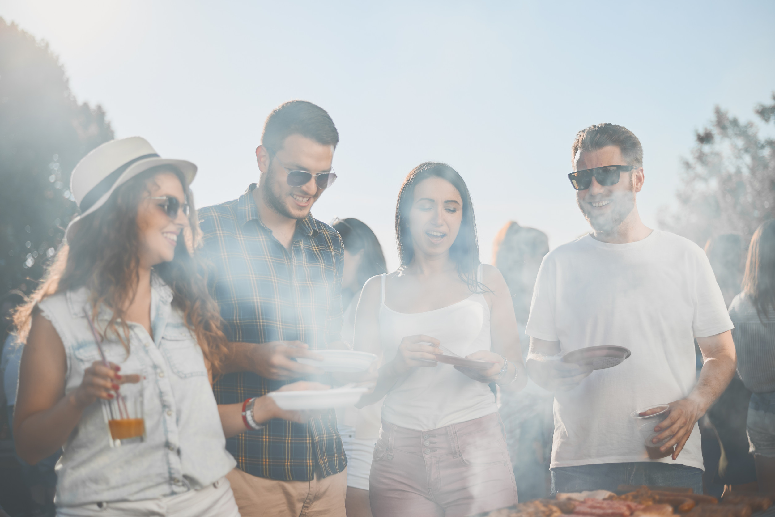 Friends drinking alcohol and eating barbecue while standing next to grill